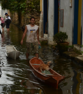 Em trecho alagado do centro histórico de Paraty, rapaz utiliza canoa caiçara para transportar pessoas e animais.